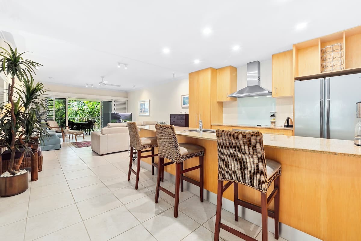 A modern kitchen with a central island, wooden bar stools, and a large refrigerator.