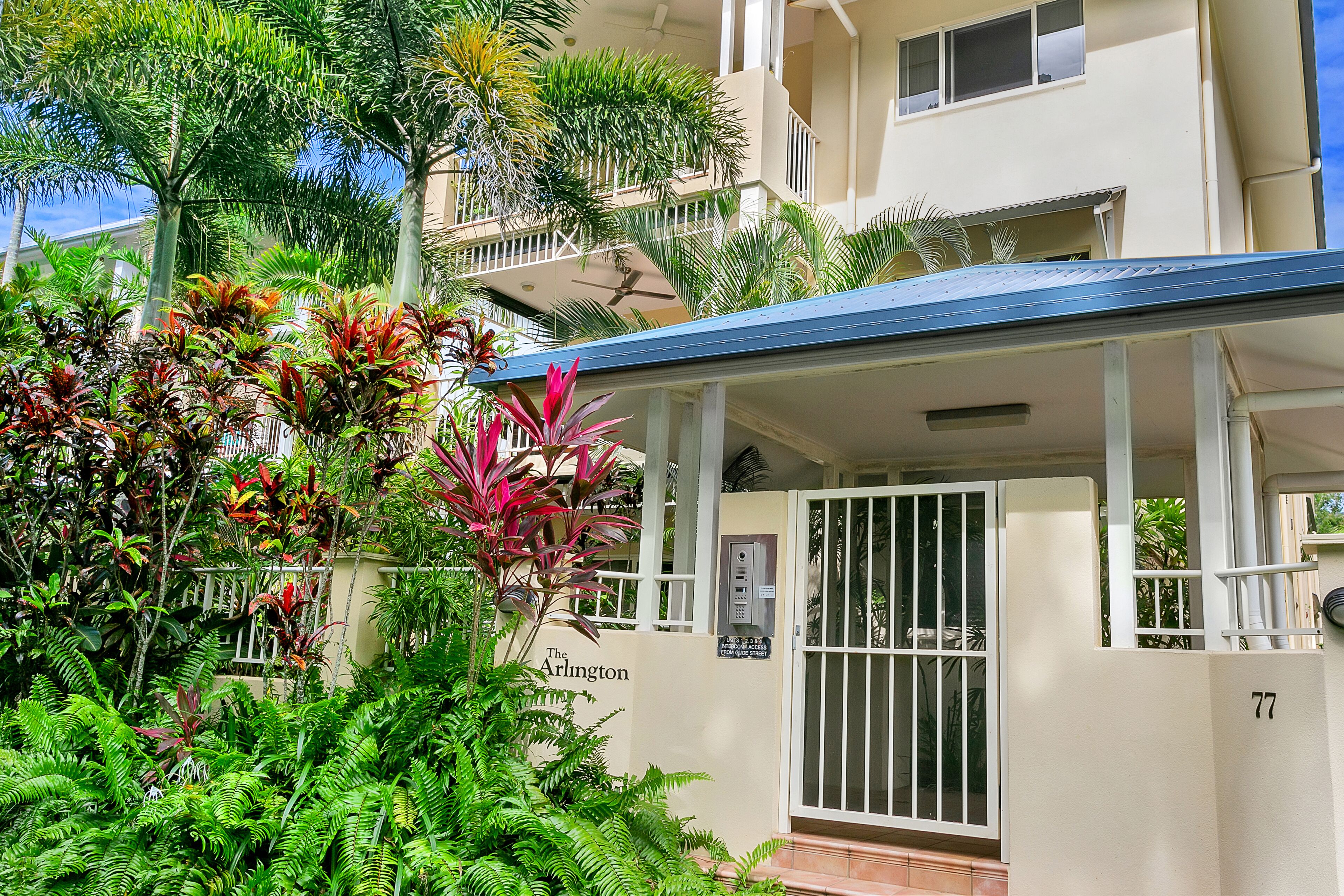 A multi-story building with a gated entrance, surrounded by lush tropical vegetation.