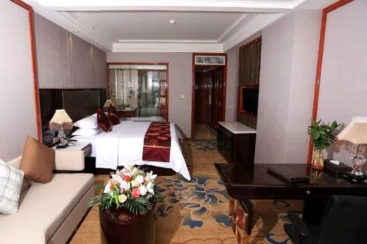 A hotel room with a bed, a desk, a sofa, and a small table with a lamp and flowers.