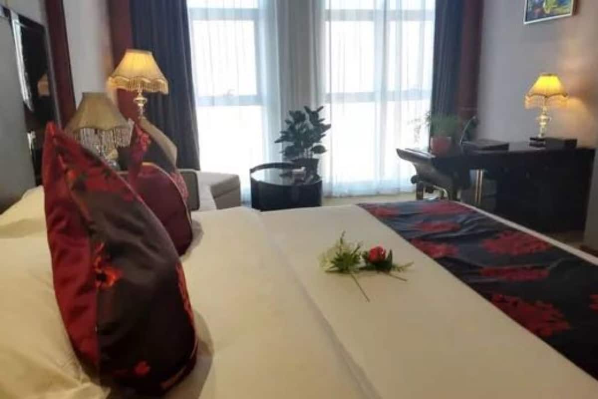 A hotel room with a bed, two lamps, a small table, and a potted plant.