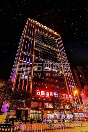 Un hotel alto con líneas verticales iluminadas y un llamativo letrero rojo que indica que es el Hotel Wushi.