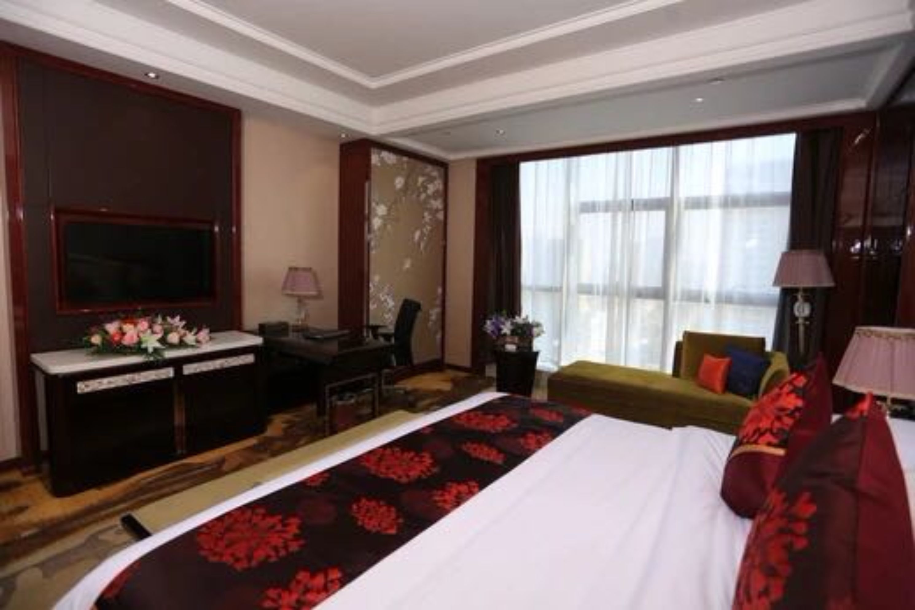 A hotel room with a large bed, a desk with a chair, a television, and a window with curtains.