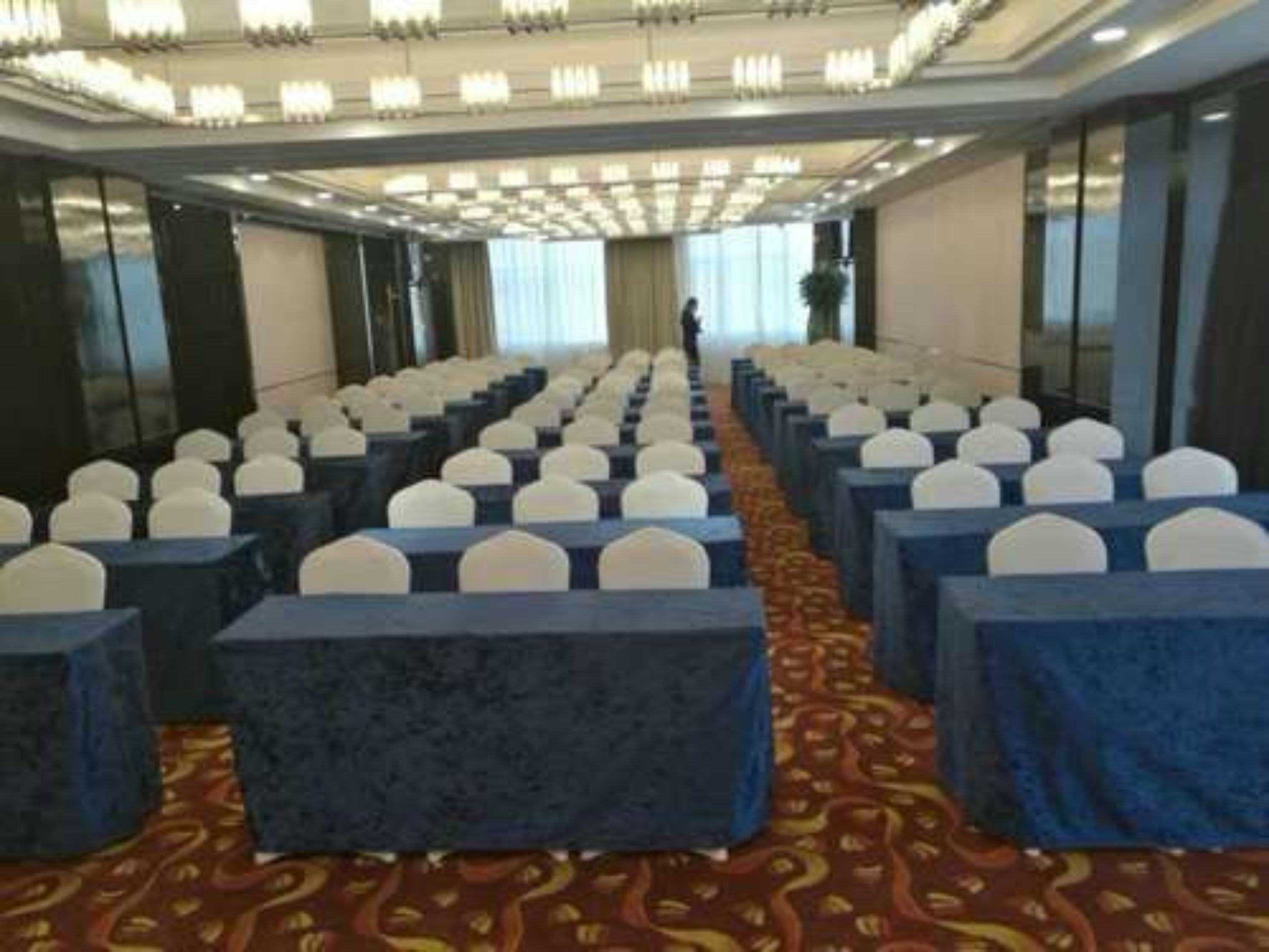 Une salle de conférence avec des rangées de tables et de chaises, une moquette à motifs et un plafond doté d’un éclairage encastré.