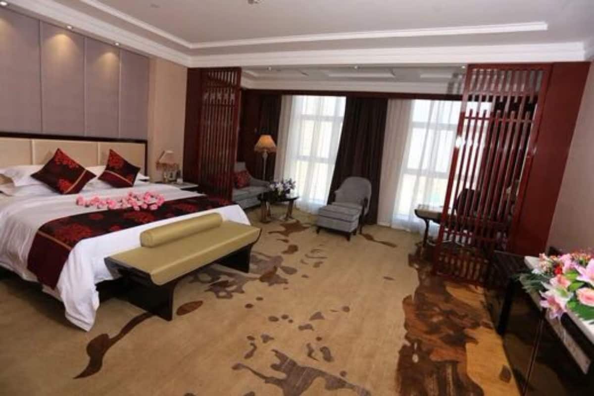 A hotel room with a large bed, a bench, a chair, and a desk with a vase of flowers.