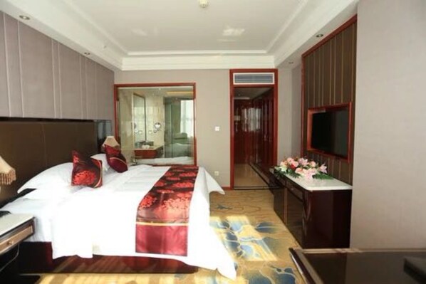 Habitación de hotel con cama, escritorio, televisión y baño visible a través de una puerta abierta.