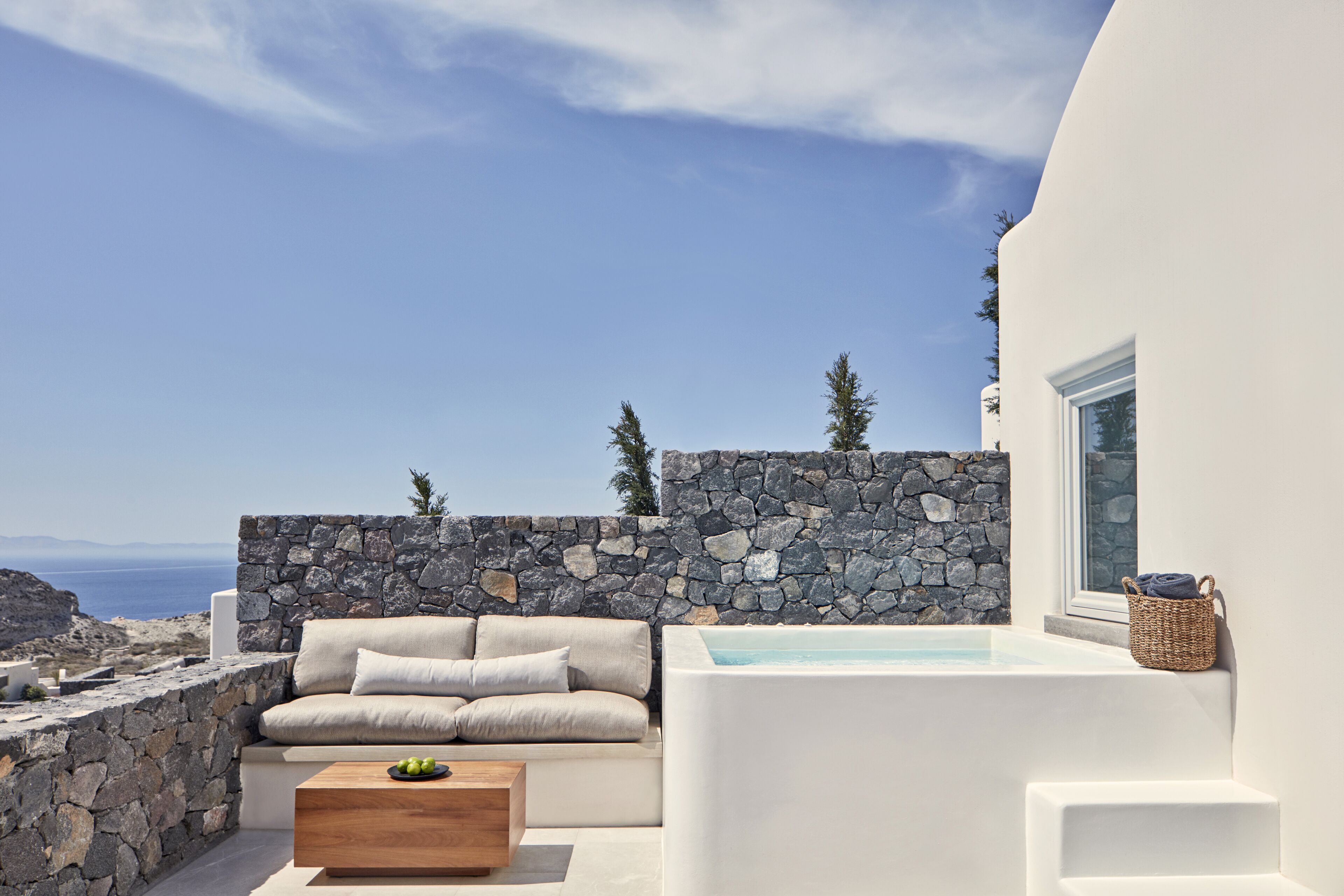 Un área de estar exterior moderna con pared de piedra, un sofá blanco y una mesa de centro de madera.