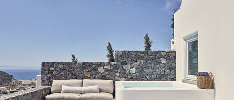 Un área de estar exterior moderna con pared de piedra, un sofá blanco y una mesa de centro de madera.