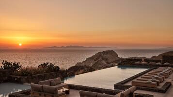 Zona de piscina con sillones de descanso y vista al océano al atardecer.