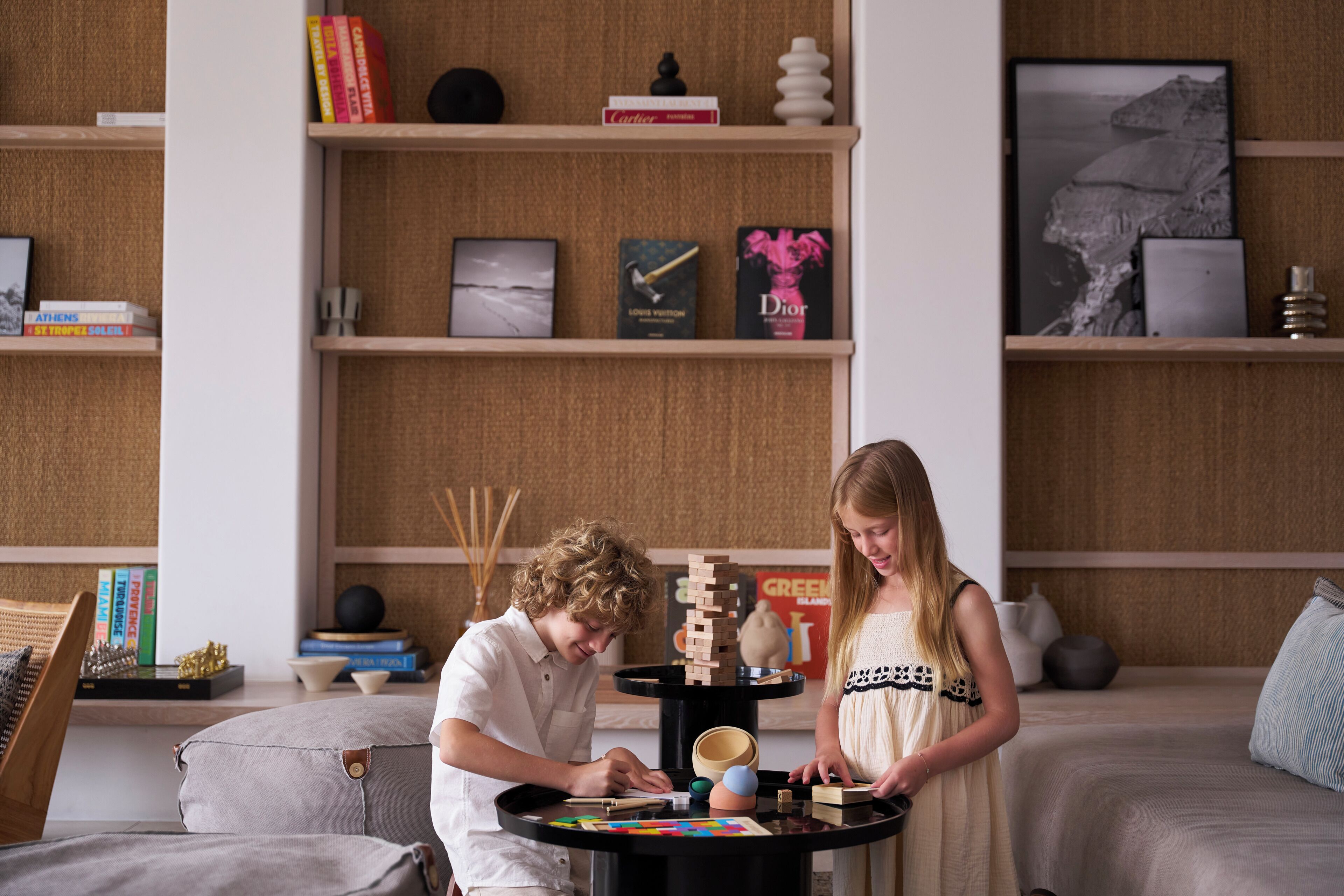 Quarto com cama, mesa redonda com brinquedos e prateleiras com livros e objetos decorativos.