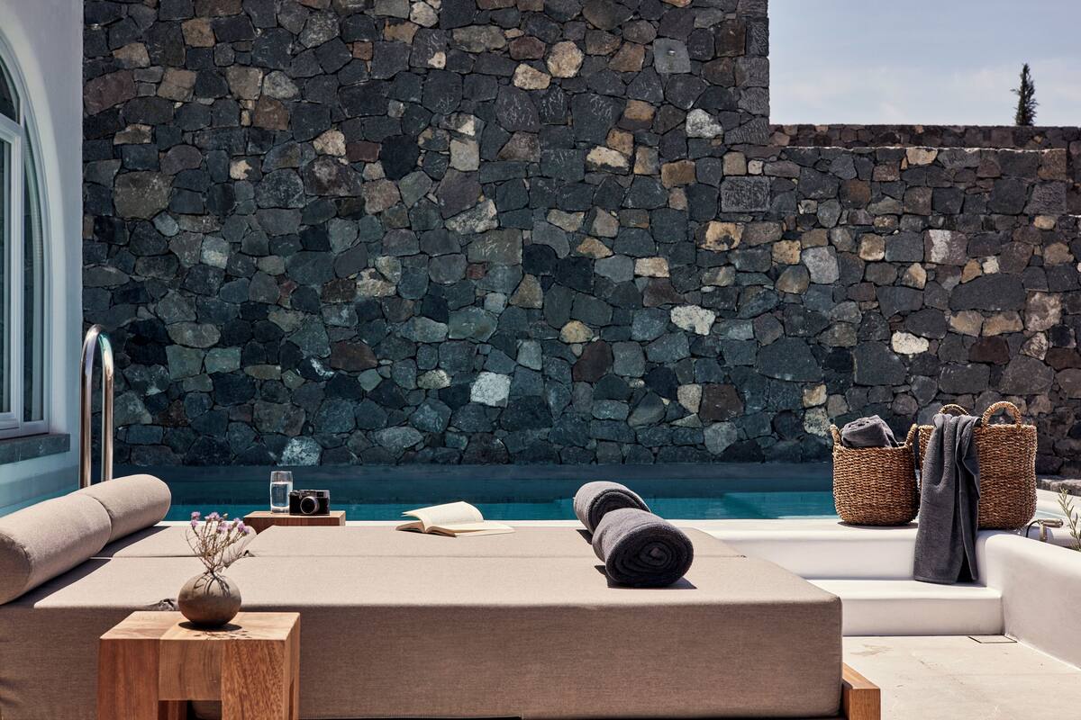 Un espace aménagé au bord de la piscine, avec un mur en pierre, des chaises longues, un appareil photo, des serviettes et des paniers.