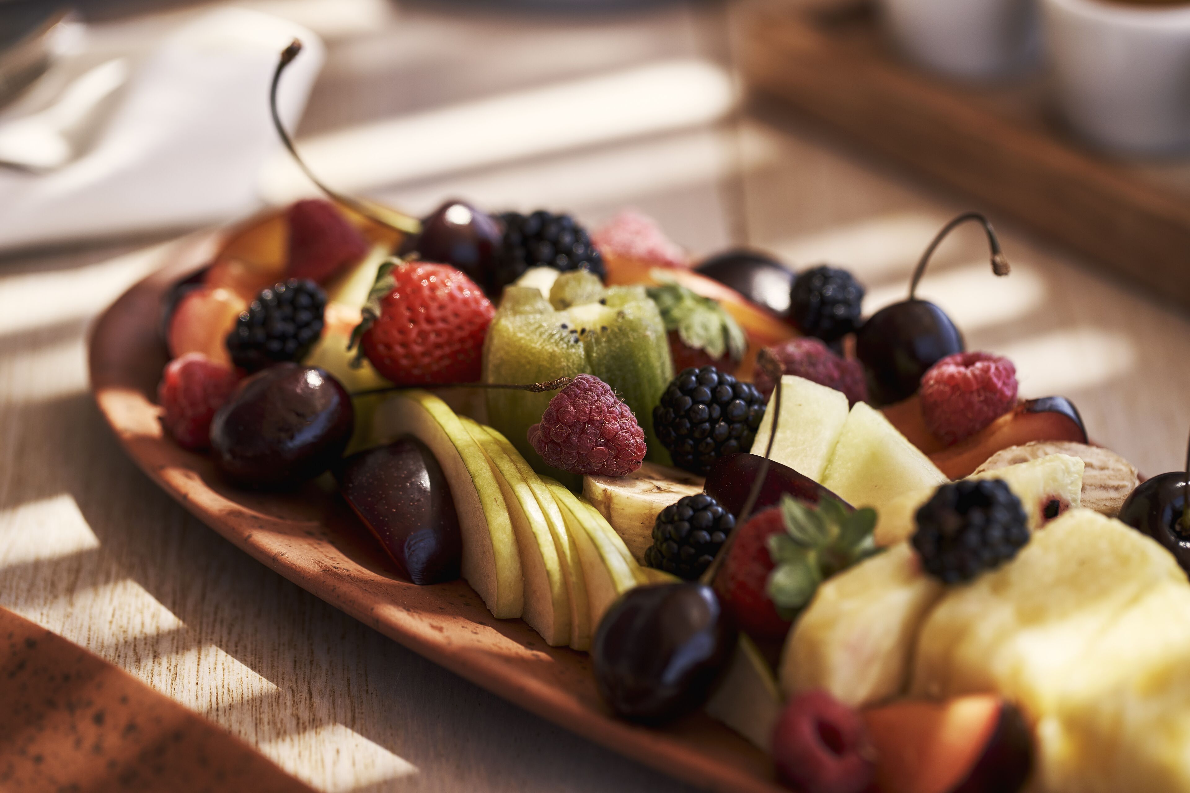 A wooden fruit platter with various fruits including apples, cherries, and berries.