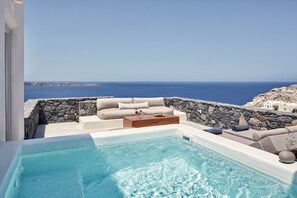 A modern outdoor pool area with a stone wall, a sofa, and a wooden coffee table.