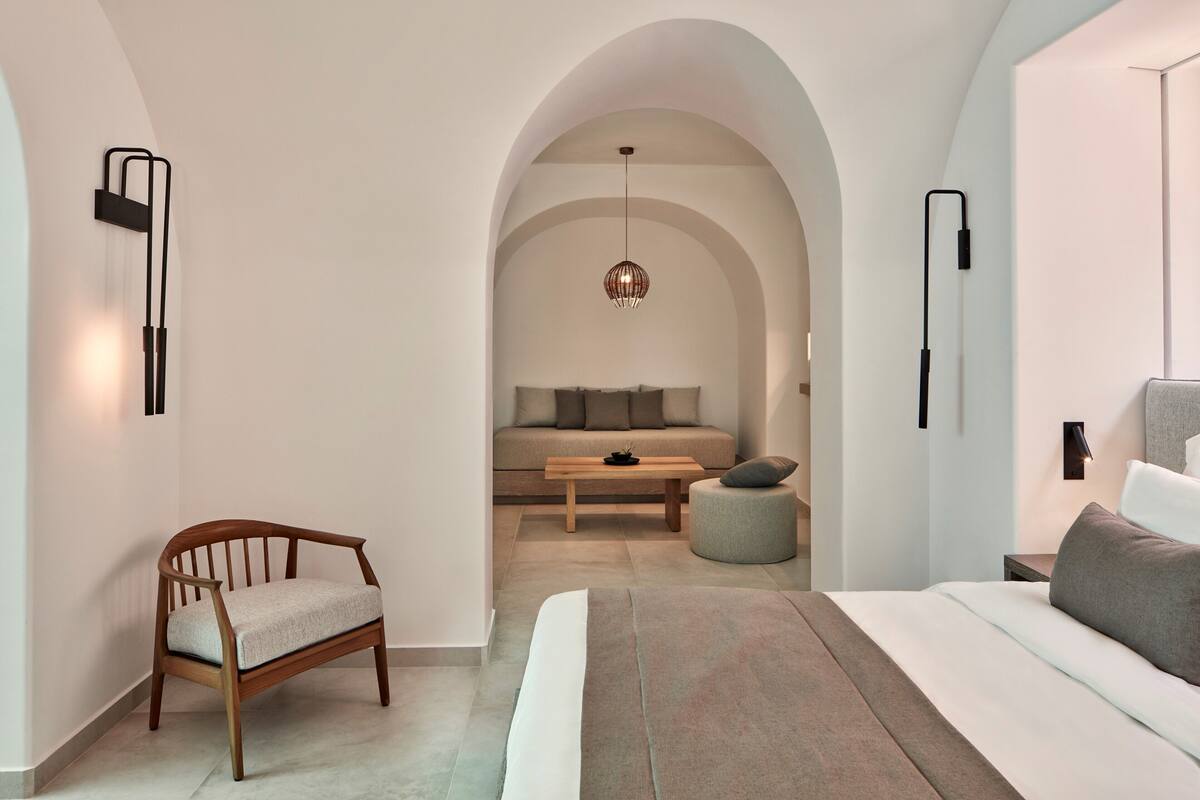 A modern bedroom with a large bed, a wooden chair, a sofa, and a small table.