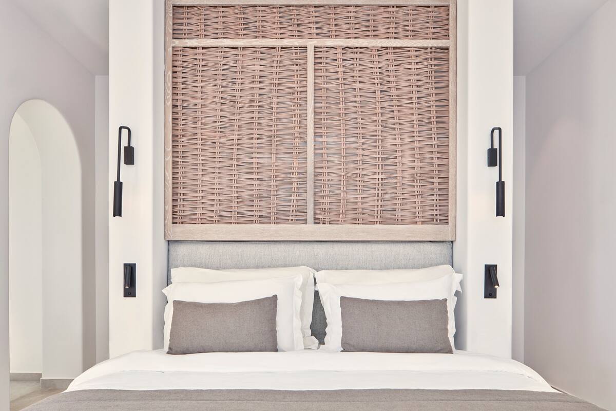 A modern bedroom with a large bed, a woven headboard, and wall-mounted lighting.