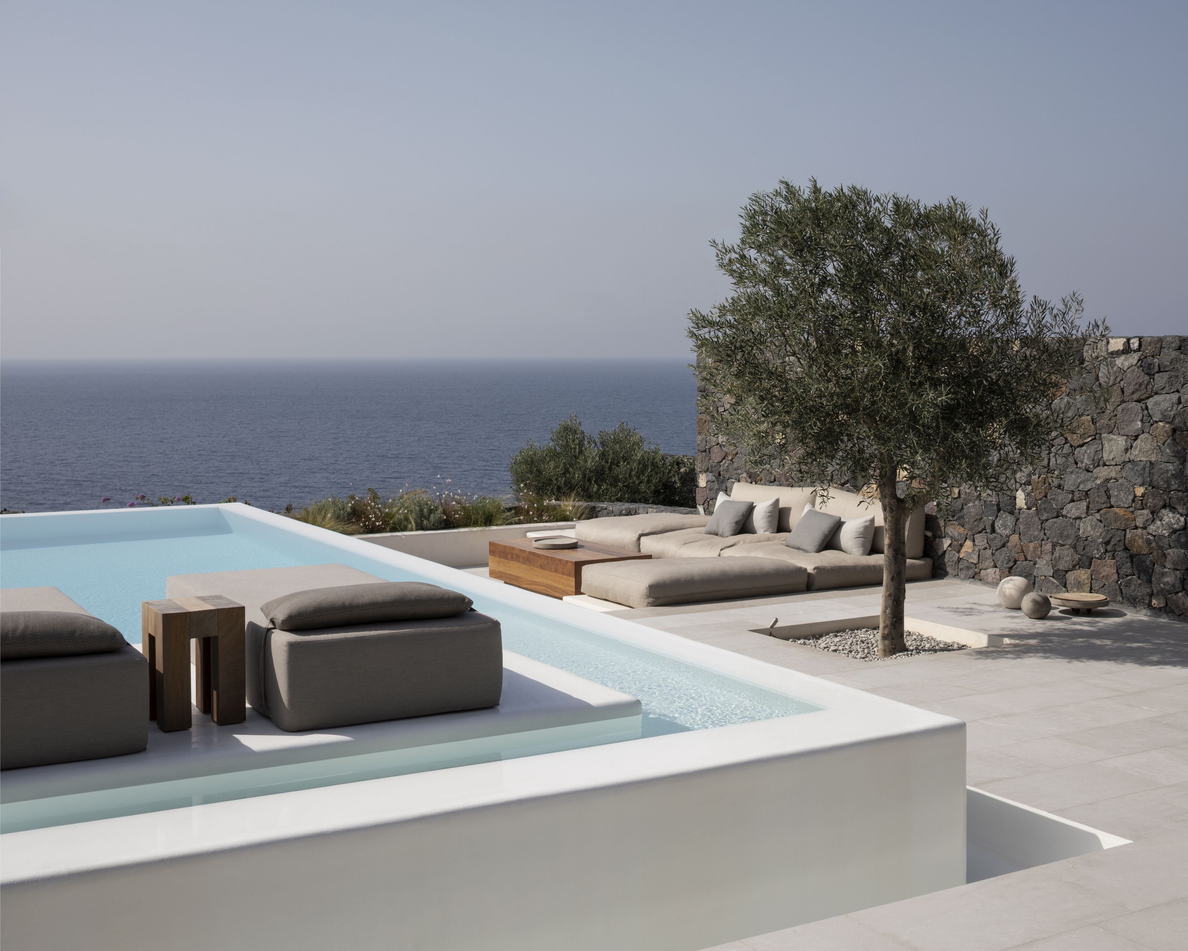 Zona de piscina exterior moderna con un muro de piedra y vistas al mar.