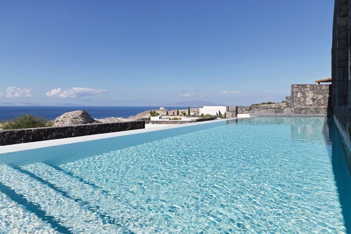 Une piscine d’un bleu éclatant, avec vue sur la mer et une structure en pierre en arrière-plan.