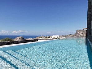 A clear blue pool with a view of the sea and a stone structure in the background.