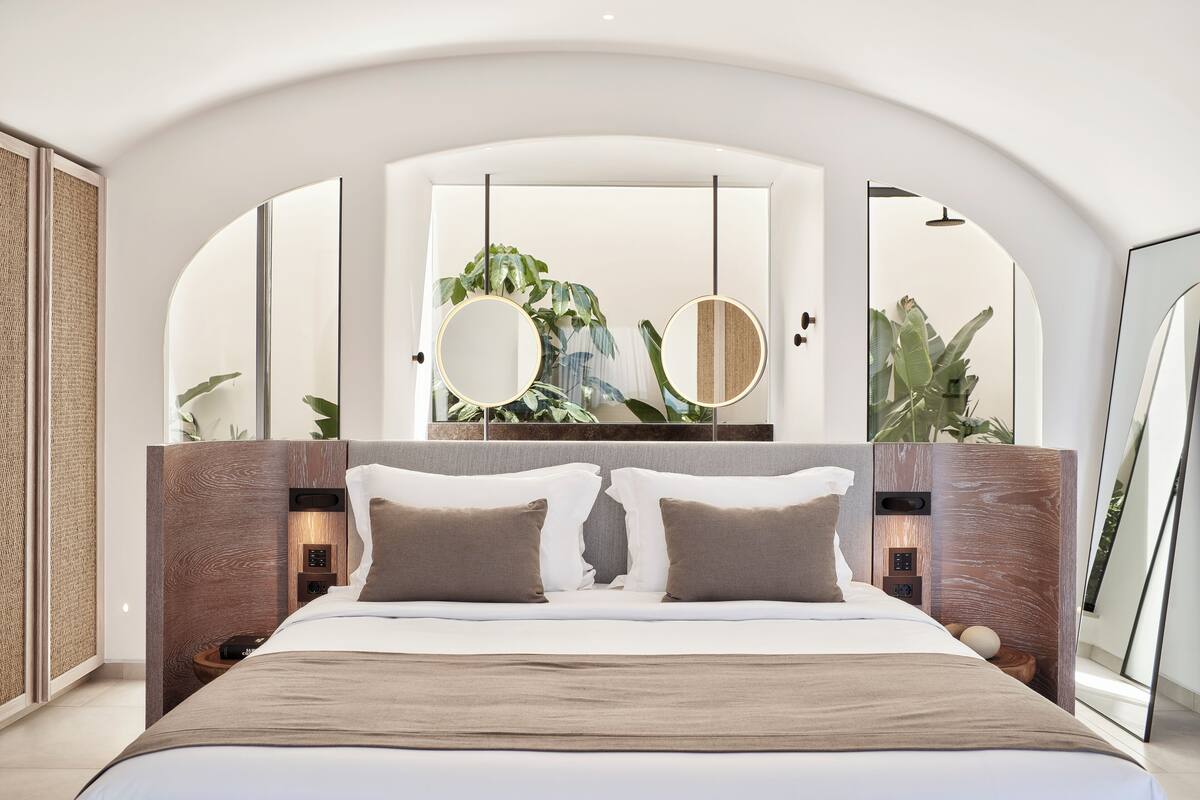 A modern bedroom with a large bed, two bedside tables, a built-in TV, and a large mirror.
