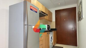 Eine kompakte Küche mit einem Hitachi-Kühlschrank, einer Mikrowelle, Holzschränken und einer Waschmaschine.