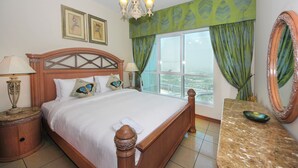 A hotel room with a large bed, a nightstand with a lamp, a dresser with a mirror, and a view of the city through the window.