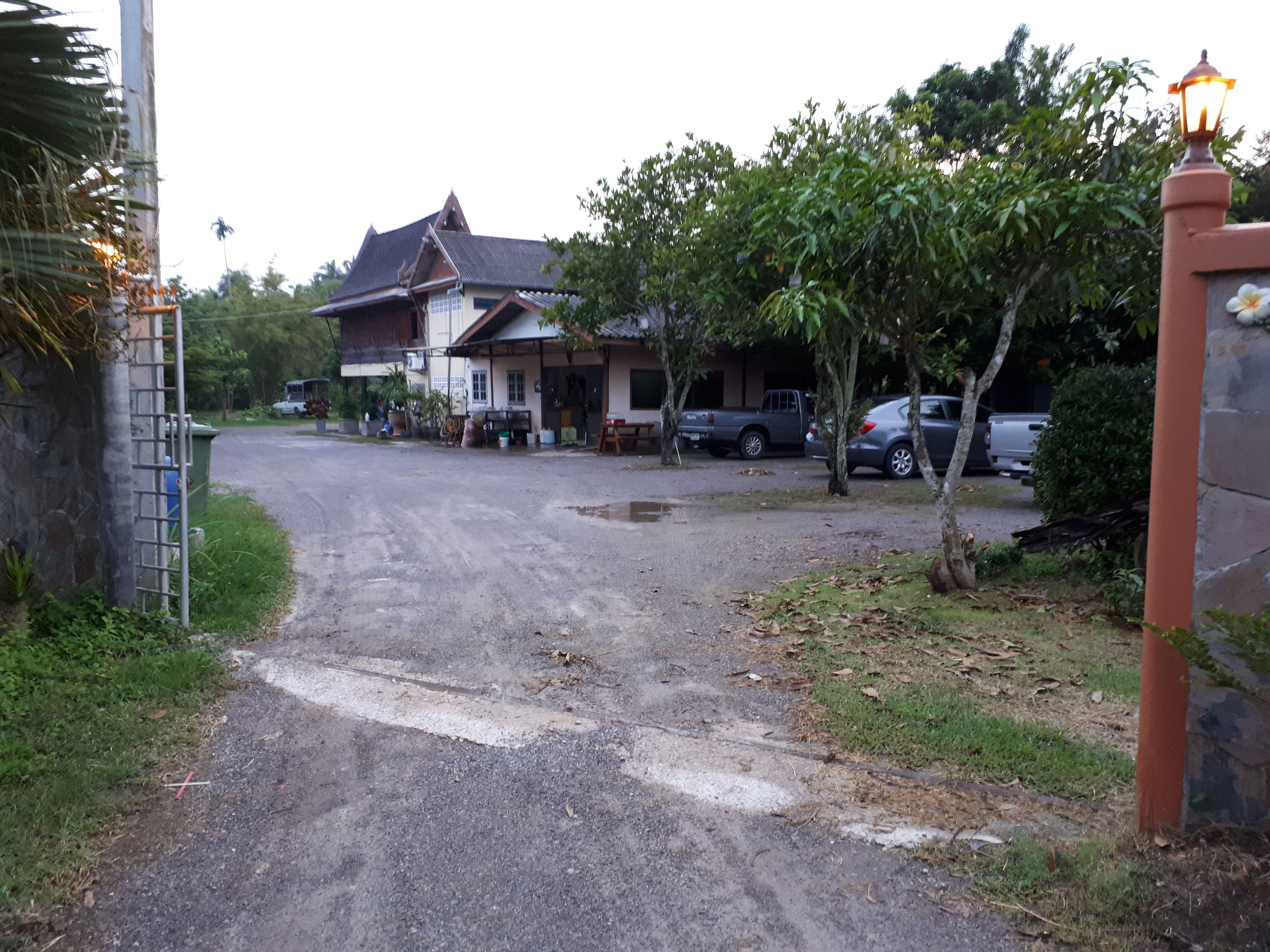 Zona residencial con una casa, coches aparcados y una entrada vigilada.