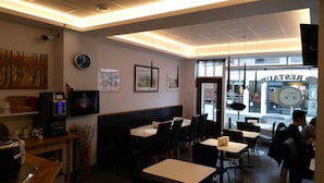 Een restaurantinterieur met tafels en stoelen, een koffiemachine en kunstwerken aan de muren.