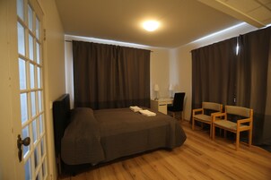 Habitación de hotel con una cama, un escritorio, dos sillas y una ventana con cortinas.