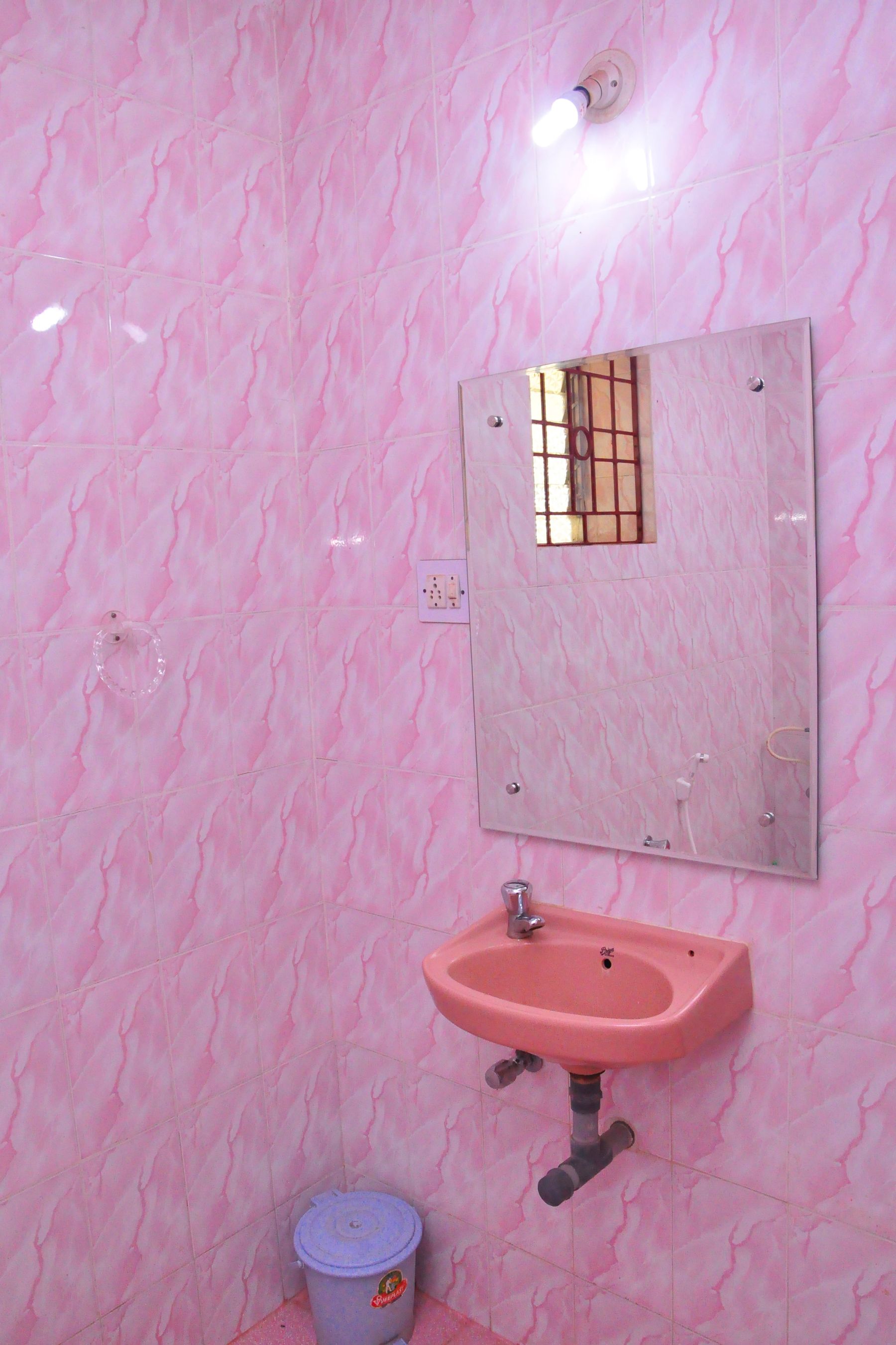Un bagno con pareti in marmo rosa, un lavandino rosa e uno specchio con una finestra.