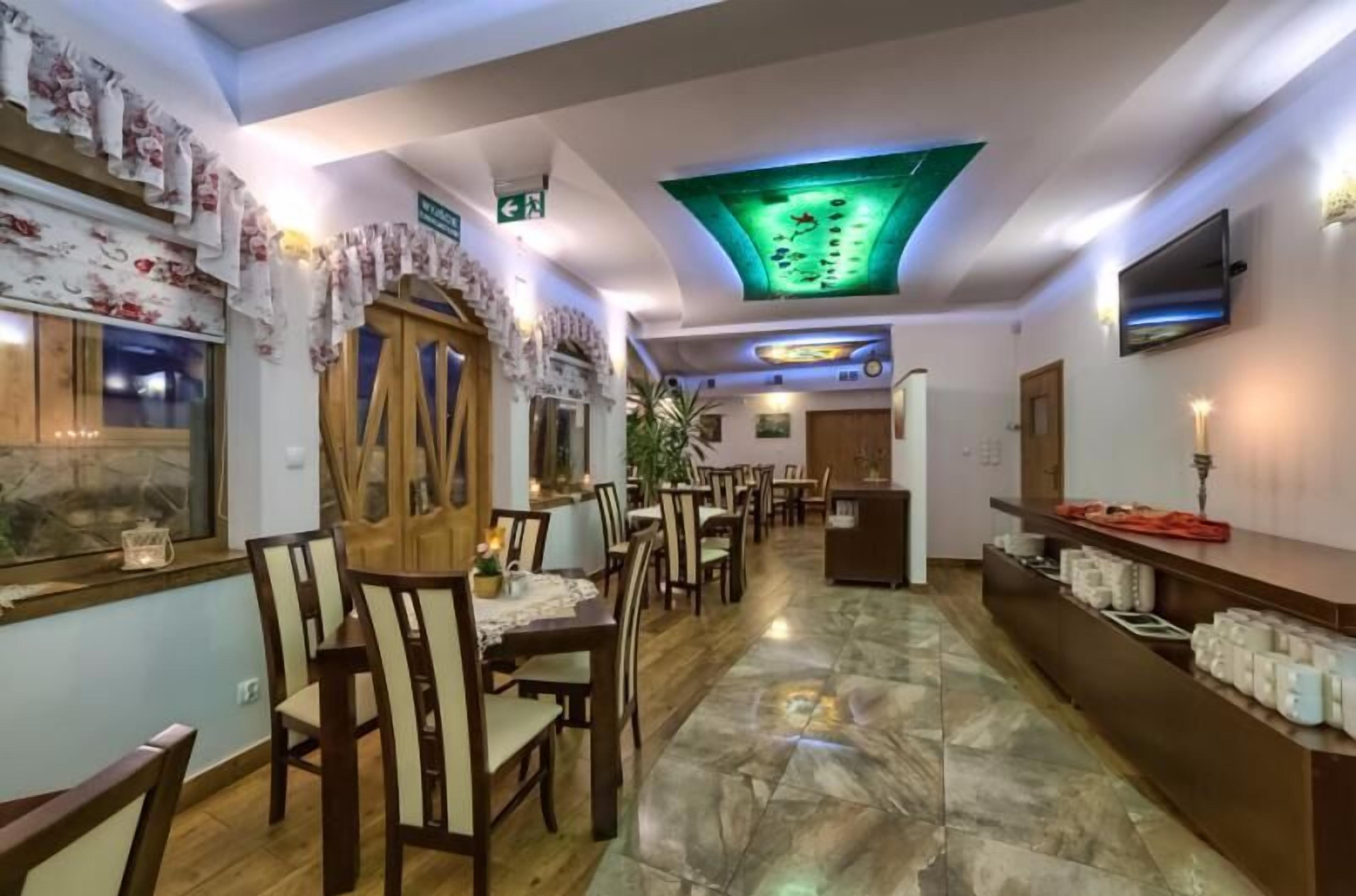 A hotel lobby with a long reception desk, multiple dining tables, and chairs.