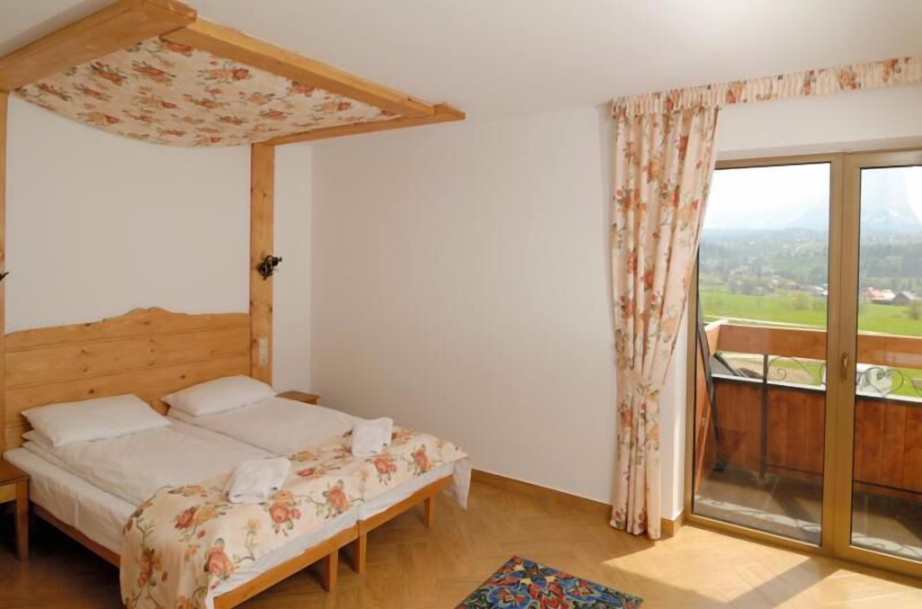 A bedroom with a wooden bed, a balcony with a view, and a floral curtain.