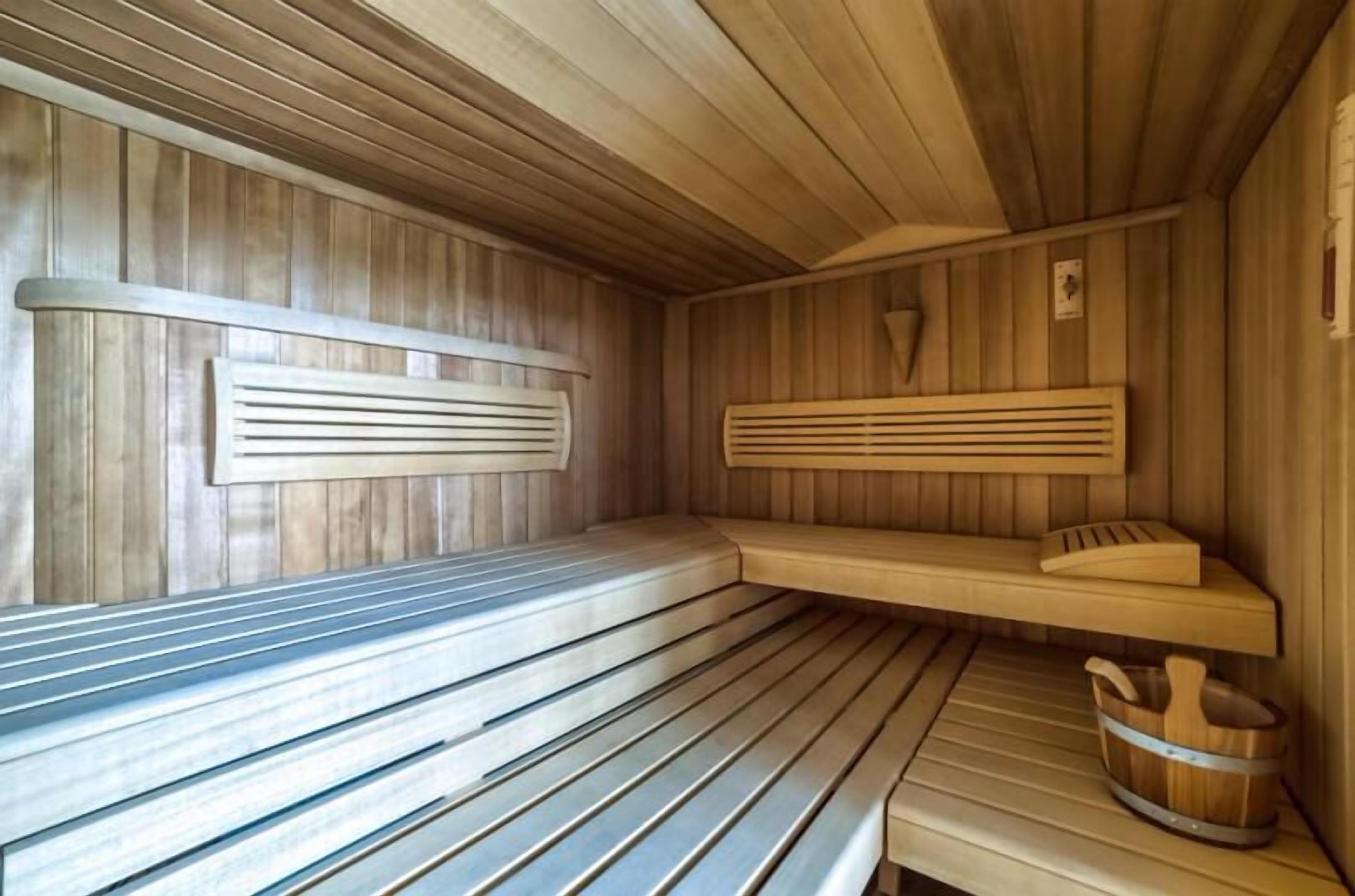 Una sauna con bancos de madera, un asiento de banco y un balde de madera.