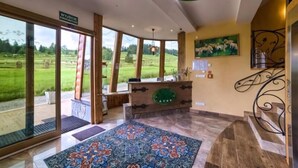 Un área de recepción con un ventanal grande que ofrece vistas a un paisaje verde, un mostrador de madera y una alfombra estampada en el suelo.