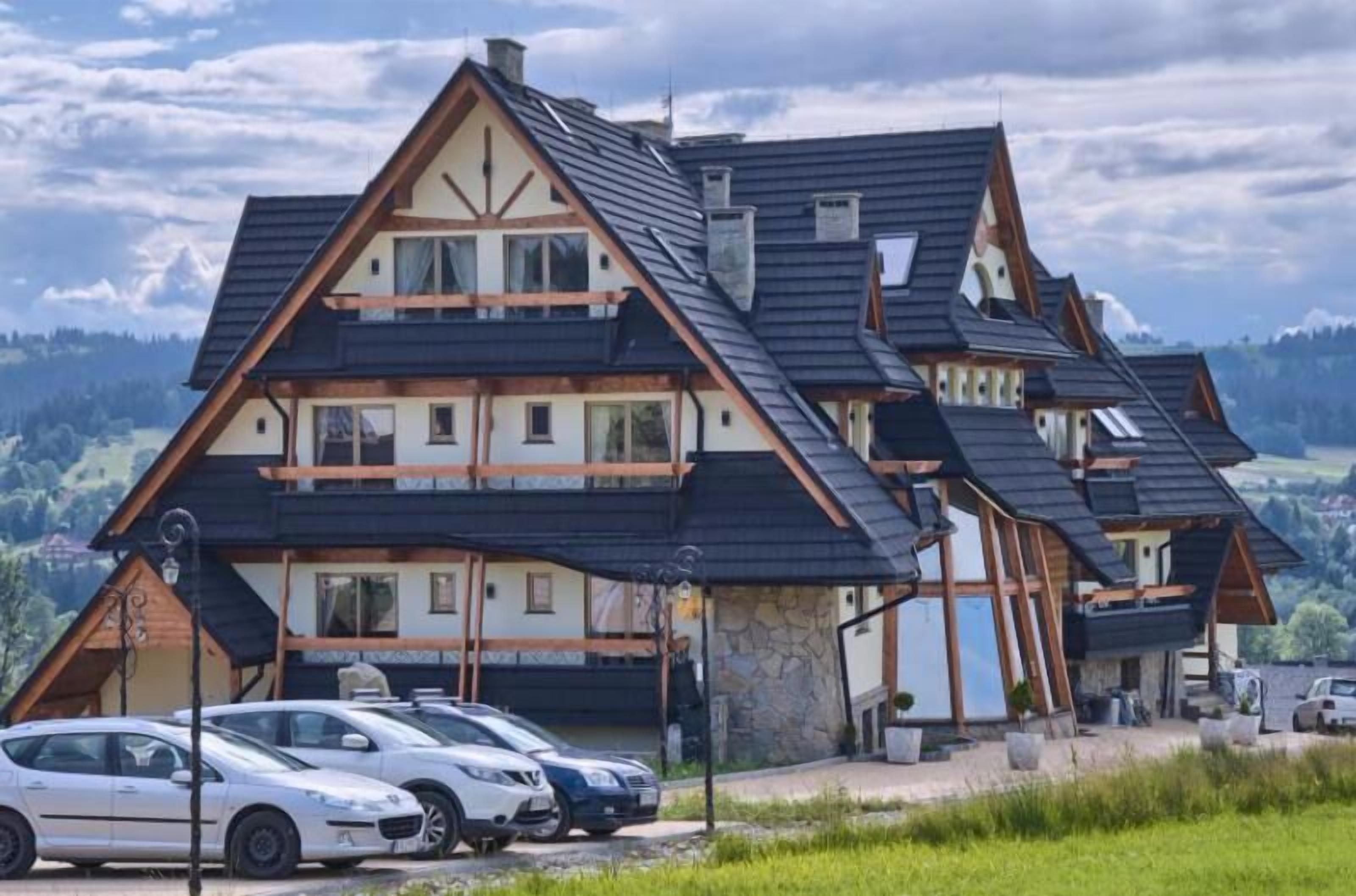 Una cabaña de varios pisos con techo inclinado, base de piedra y un estacionamiento con varios automóviles.
