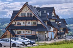 Um chalé de vários andares com telhado íngreme, base de pedra e um estacionamento com vários carros.