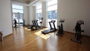 A spacious gym with multiple exercise machines, large windows, and a wooden floor.