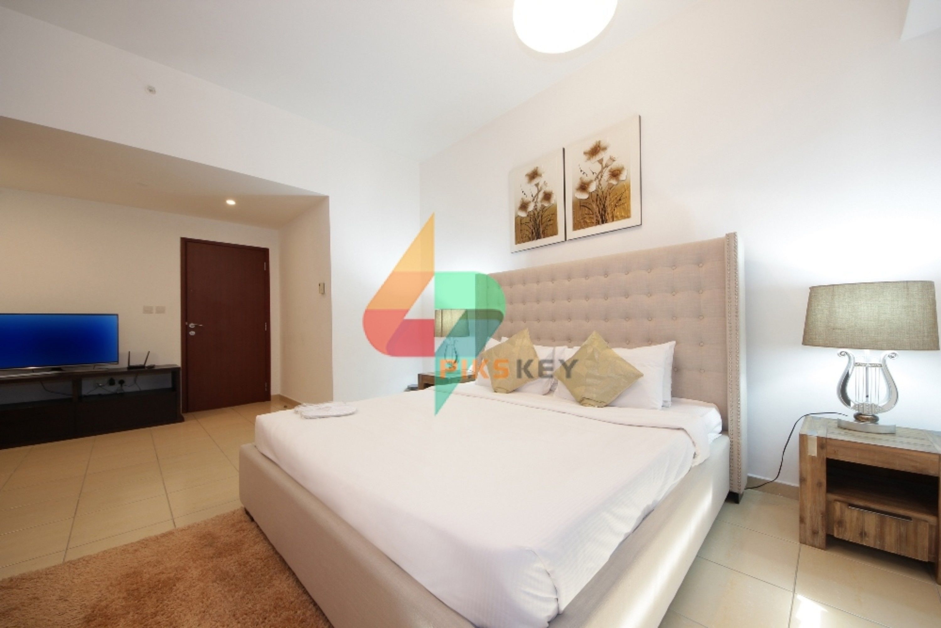 A modern hotel room with a large bed, a TV, and a wooden nightstand.