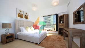A modern bedroom with a large bed, a nightstand, a wooden bench, and a view of a cityscape through a large window. - Piks Key - Sadaf 4 (Dubai)