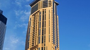 Ein hohes, beige Gebäude mit moderner Architektur, zahlreiche Fenster und eine markante Dachkonstruktion.
