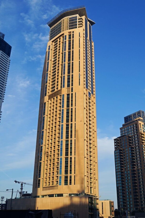 A tall, beige-colored high-rise building with a modern architectural design, featuring numerous windows and a prominent rooftop structure.