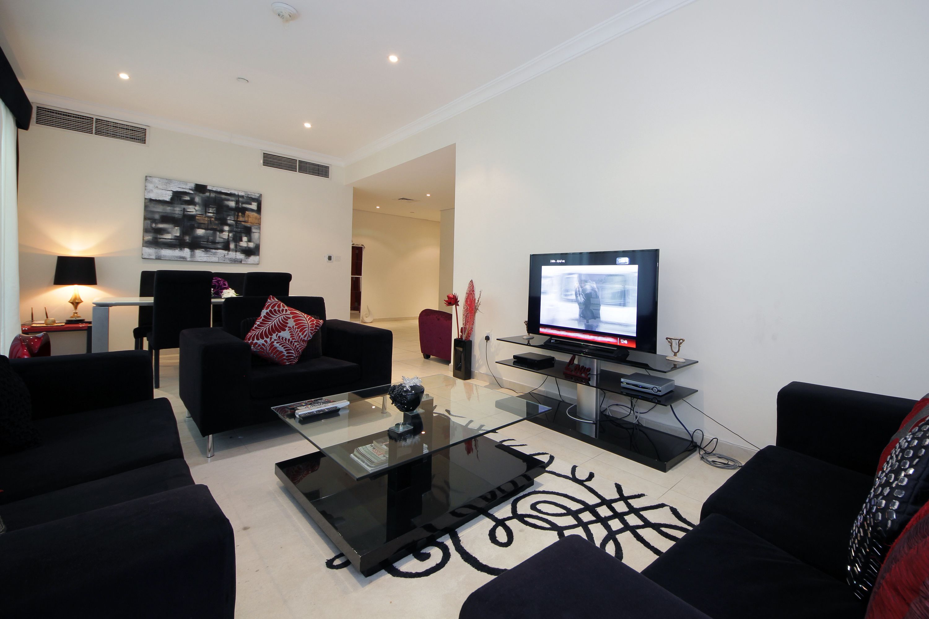 A modern living room with black sofas, a glass coffee table, a flat-screen TV, and a minimalist decor.