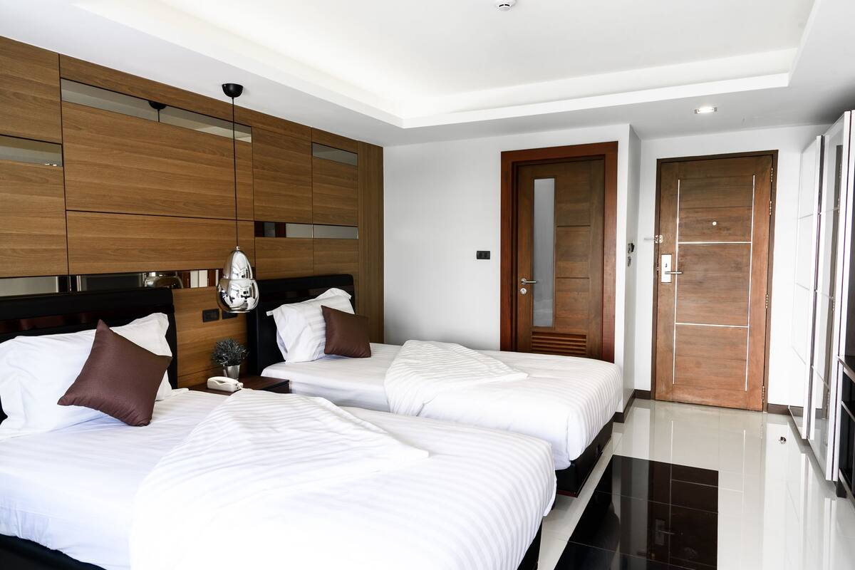A hotel room with two beds, wooden headboards, a nightstand, a mirror, and a door with a handle.