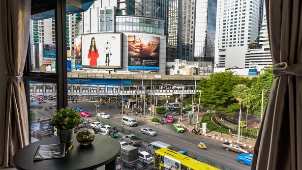A view from a window overlooking a busy urban street with tall buildings and a billboard. - The Connex Asoke (Bangkok)