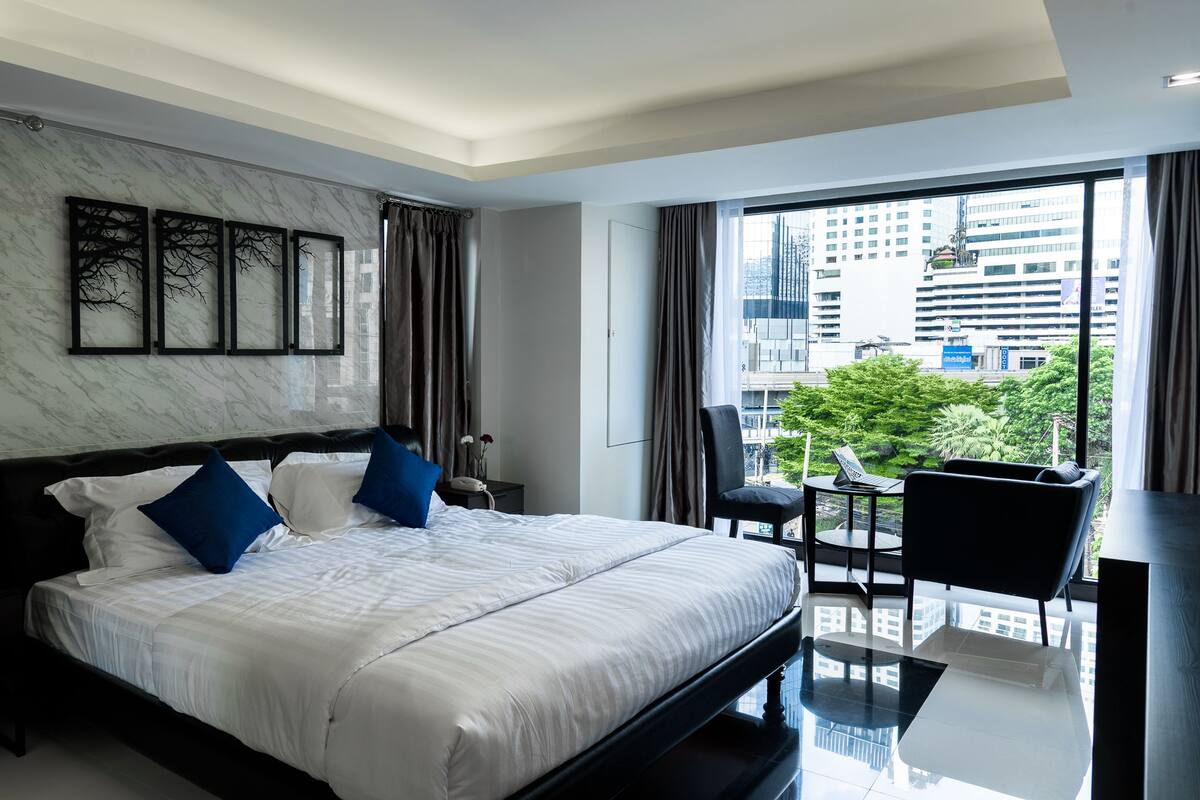 A modern hotel room with a large bed, a dining area, and a view of the city.