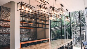 A modern bar area with a wooden counter, multiple hanging light fixtures, and a view of a metal structure outside. - The Connex Asoke (Bangkok)