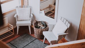 Esquina de una habitación con dos sillas blancas, una cesta de mimbre con zapatos y un radiador.