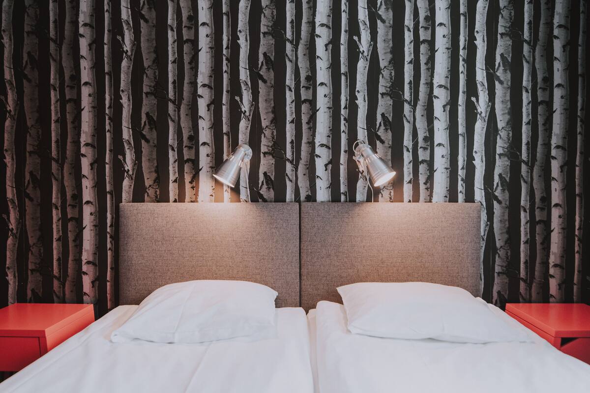 Un lit double avec deux tables de chevet, une tête de lit dotée d’un luminaire et un mur orné d’un motif représentant un bouleau.