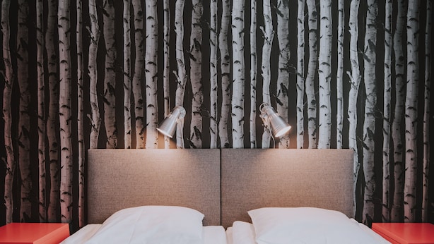 Una cama doble con dos mesitas de noche, cabecero con lámpara y pared decorada con un diseño de abedules.