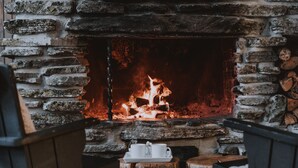 Una chimenea de piedra con fuego encendido, rodeada de muebles de madera rústica.