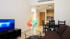 A living room with a flat-screen TV, a glass coffee table, a brown sofa, and a dining area with chairs and a table. - Piks Key - Mayfair Residency (Dubai)