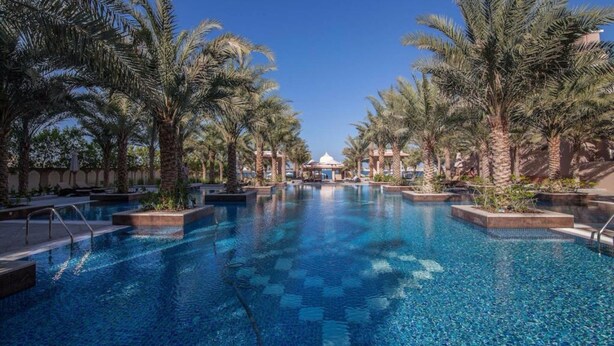 A swimming pool surrounded by palm trees, with a clear blue sky above. - Piks Key - Grandeur Residences (Dubai)